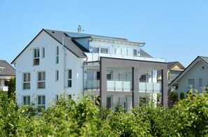 A modern multi-story residential building with balconies, large windows, and a flat roof.