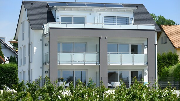 En moderne bygning i to etager med balkon, store vinduer og solpaneler på taget.