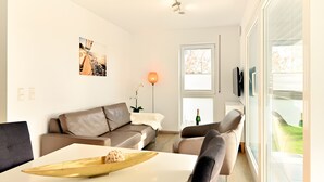 En moderne stue med sofa, lænestole, sofabord og et stort vindue.