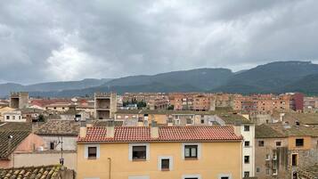 A cityscape with historic buildings, terracotta roofs, and a mountainous backdrop.