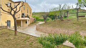 A building with a stone wall, a paved pathway, and a grassy area with trees. - Medieval House in the Heart of Montblanc (Montblanc)
