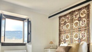 A bedroom with a large bed, a nightstand, a window with a view of the sea, and a decorative tapestry. - Medieval House in the Heart of Montblanc (Montblanc)