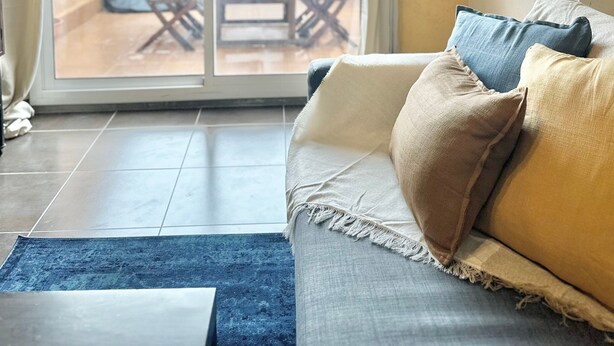 A living room with a sofa, a blue rug, and a sliding glass door leading to an outdoor patio with a table and chairs. - Medieval House in the Heart of Montblanc (Montblanc)