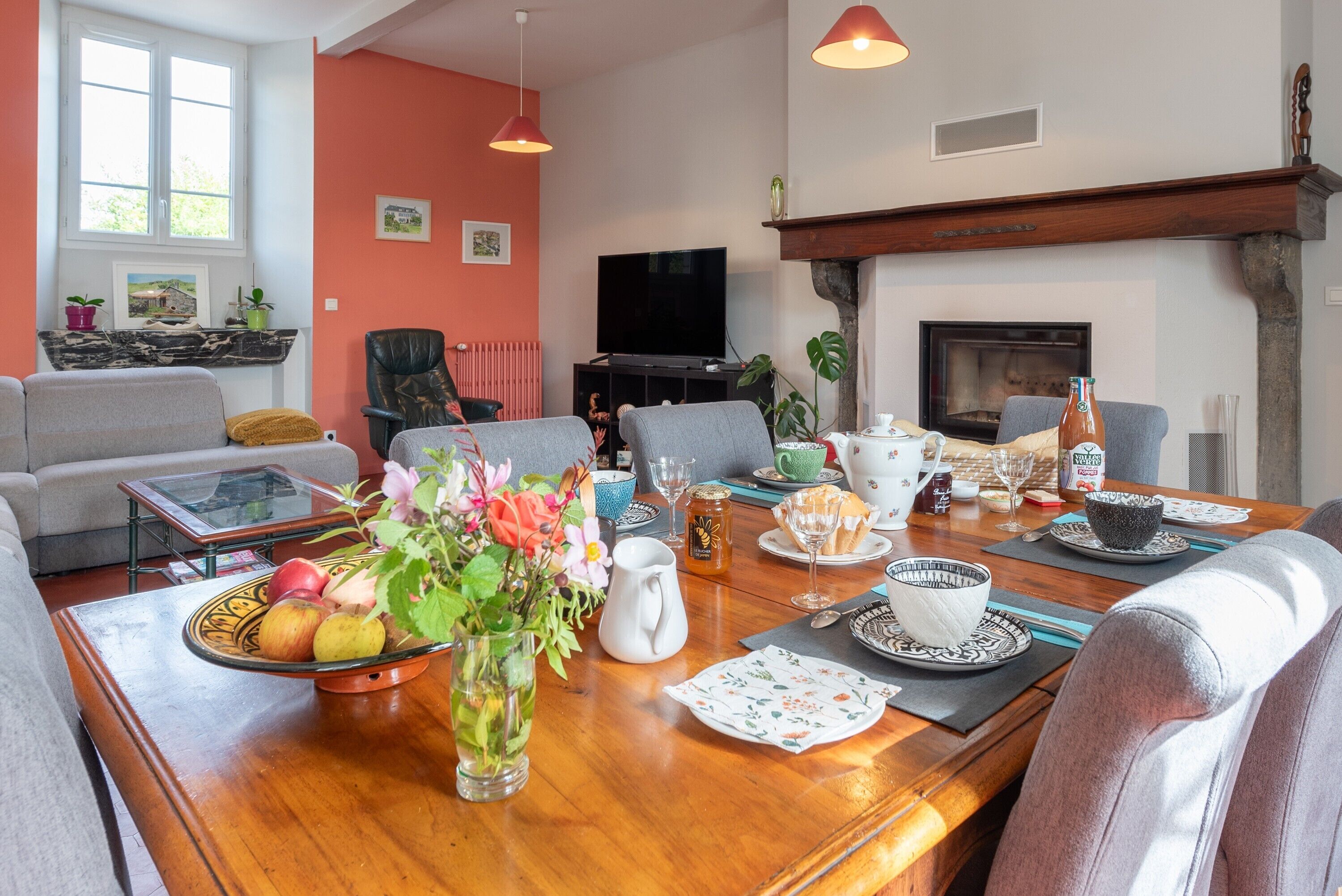 A living room with a wooden dining table set for a meal, a television, and a fireplace.