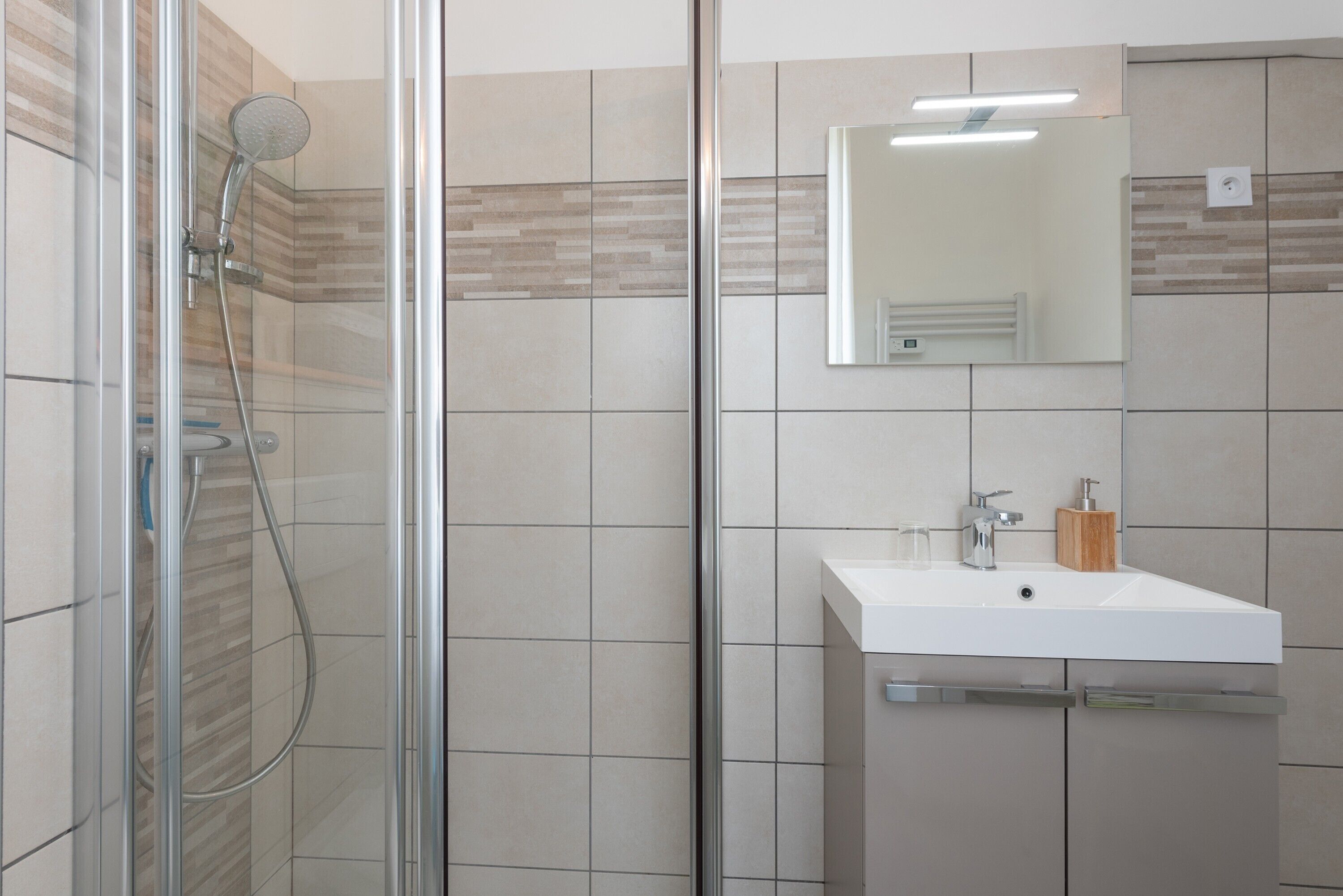 Une salle de bain moderne avec une douche à parois de verre, un lavabo blanc et un miroir au-dessus.