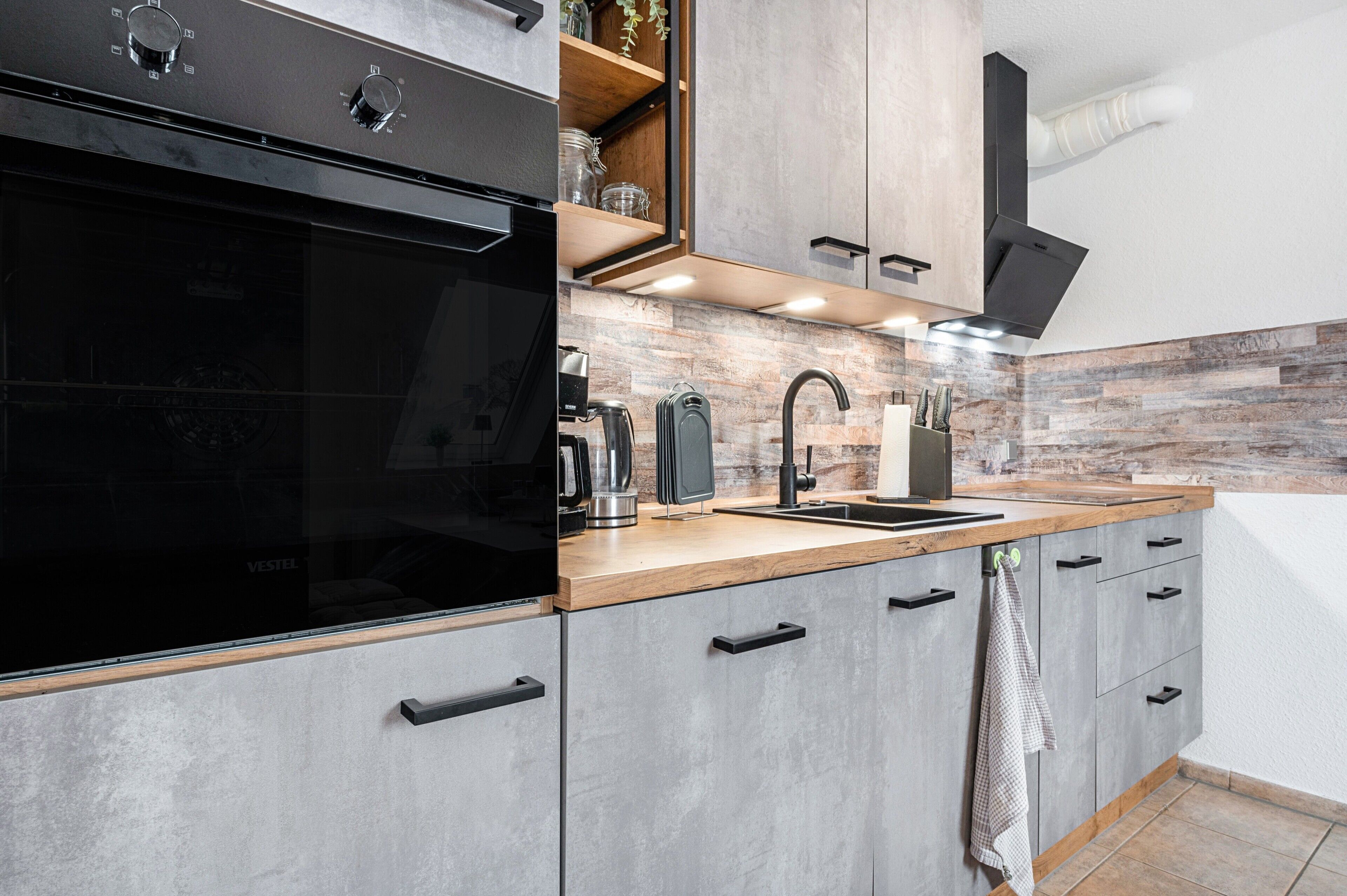 A modern kitchen with a black oven, wooden countertop, and grey cabinets.