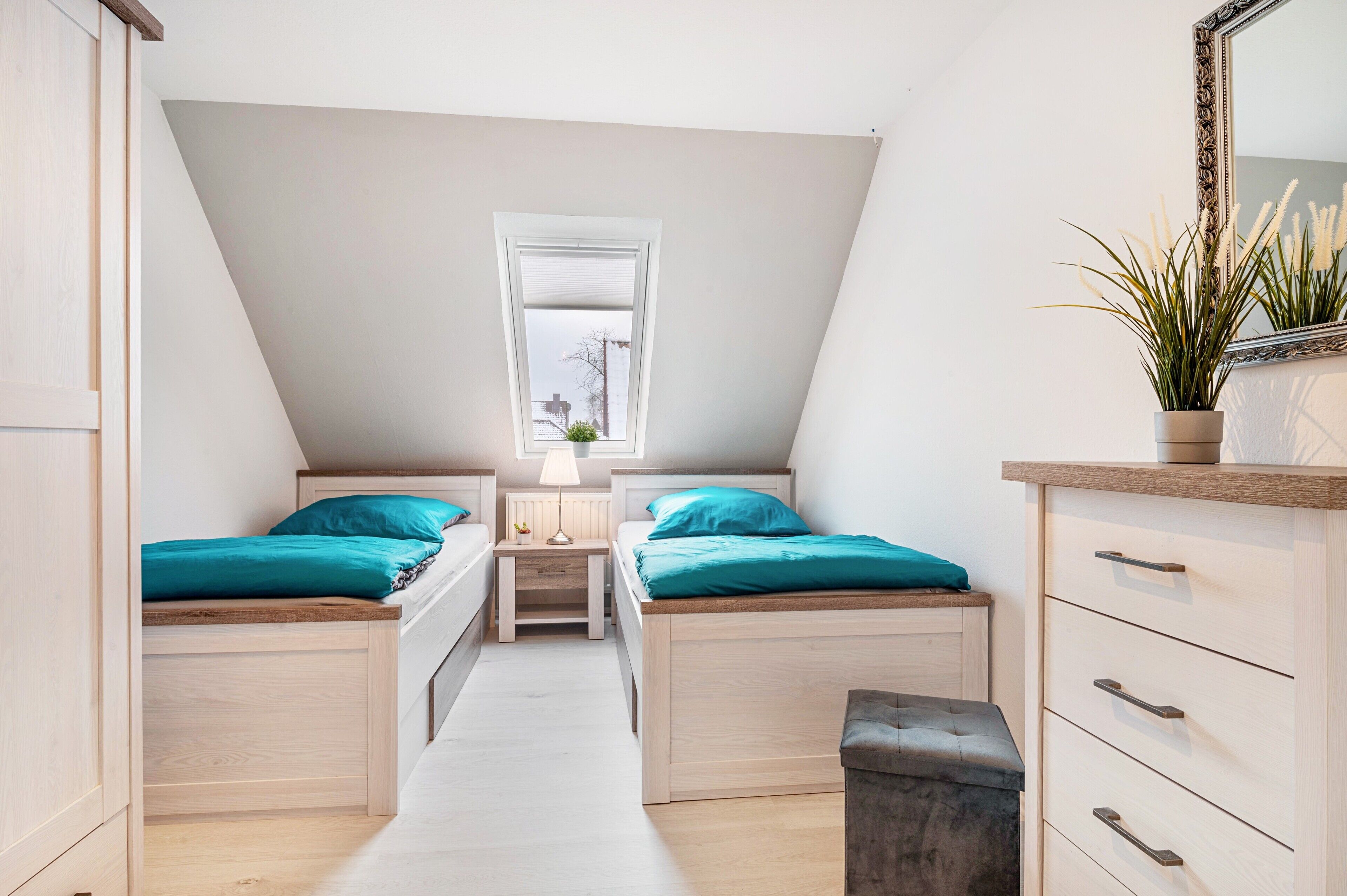 A bedroom with two beds, a window, a dresser, and a plant.