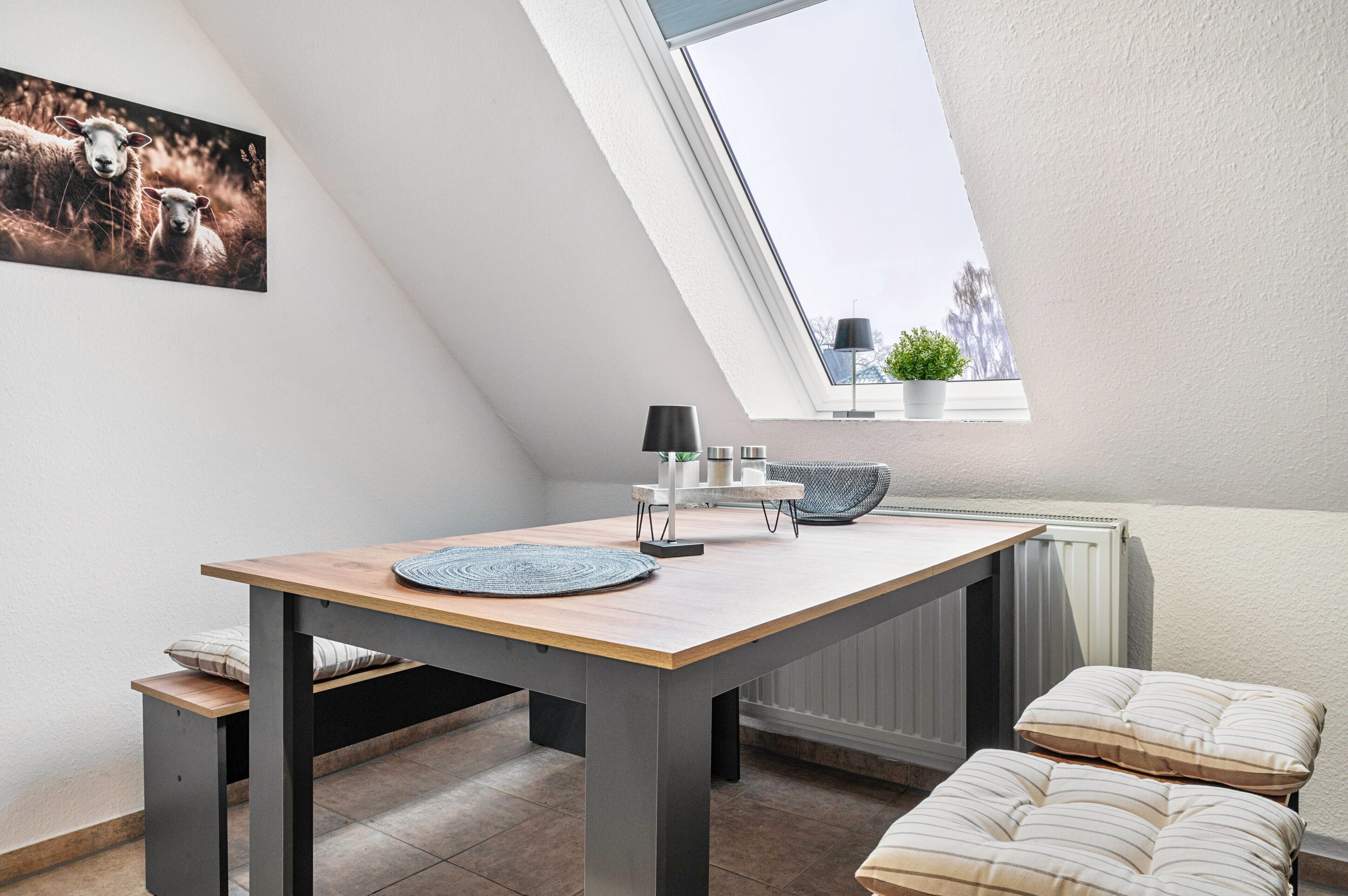 A modern loft bedroom with a skylight, a dining area with a table and chairs, and a cozy seating area with cushions.