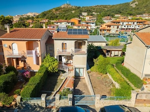 A residential area with houses featuring balconies, solar panels, and a hillside in the background.