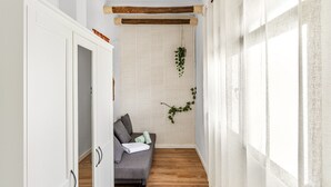 A narrow hallway with a wooden floor, a grey sofa with cushions, a hanging plant, and a white door. - Village house, 100m from the beach, with Wi-Fi and air conditioning (Estepona)