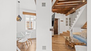 A spacious living area with a wooden staircase, white walls, and a dining area with a glass table and chairs. - Village house, 100m from the beach, with Wi-Fi and air conditioning (Estepona)