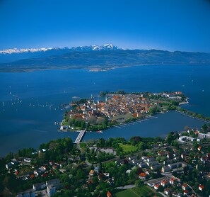 An aerial view of a coastal town with a prominent island, a bridge, and a mountain range in the background.