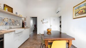 Une cuisine avec des meubles blancs, un pare-feu en carrelage et une table à manger en bois, accompagnée d’une chaise jaune.