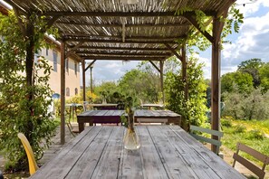Una mesa de madera con un florero, una pérgola y vistas a la vegetación y un edificio al fondo.