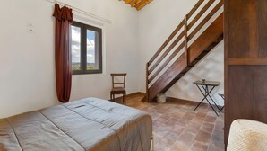 Une chambre à coucher comprenant un lit, une chaise, une petite table, une fenêtre avec des rideaux, un escalier en bois et une vue sur l’extérieur.