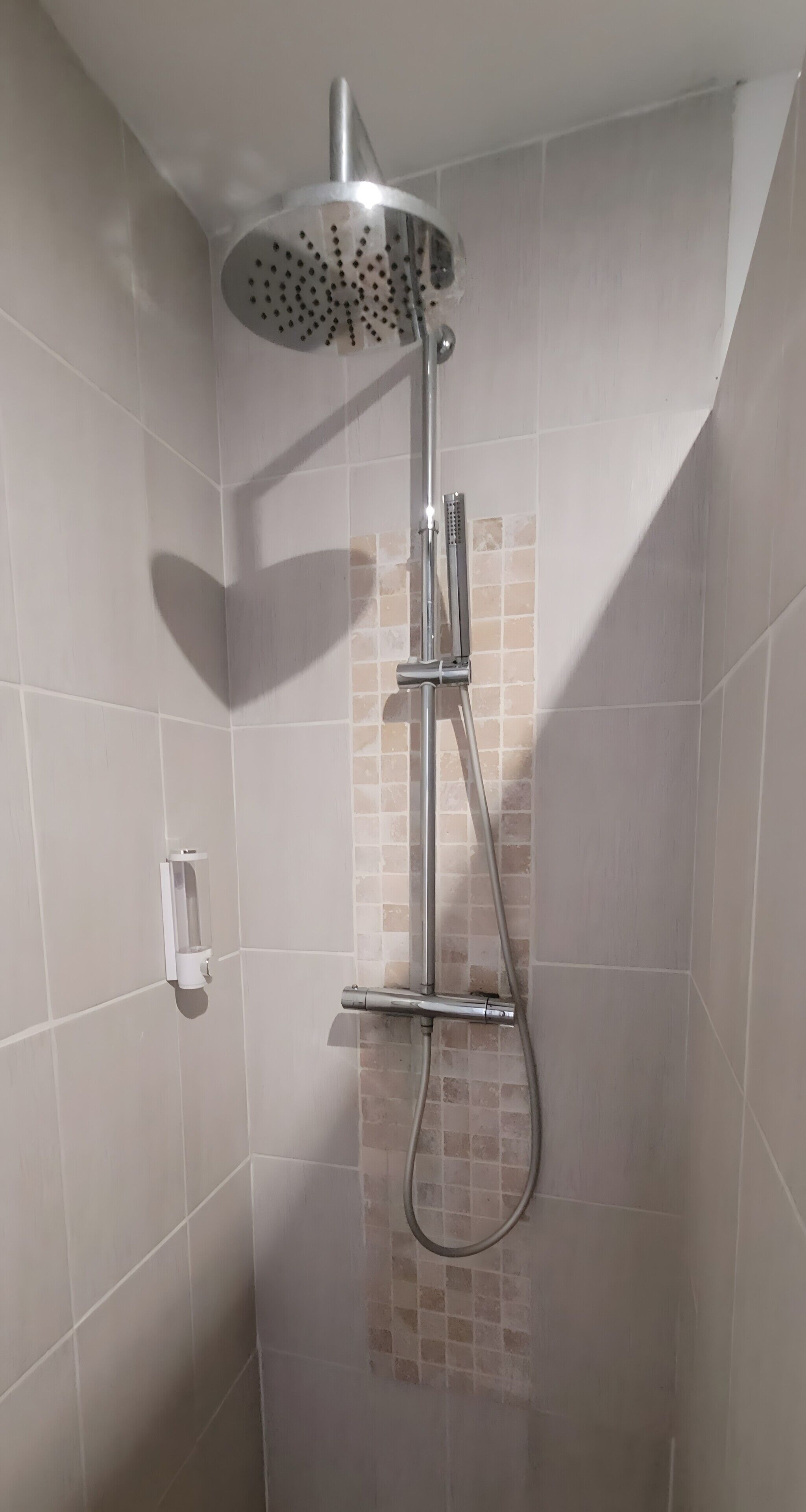 Ducha con cabezal de ducha tipo lluvia y cabezal de ducha de mano, paredes con azulejos y diseño en esquina.