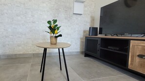 Un salon avec un mur en briques, une table ronde ornée d’une plante, un canapé bleu, un téléviseur et un meuble.