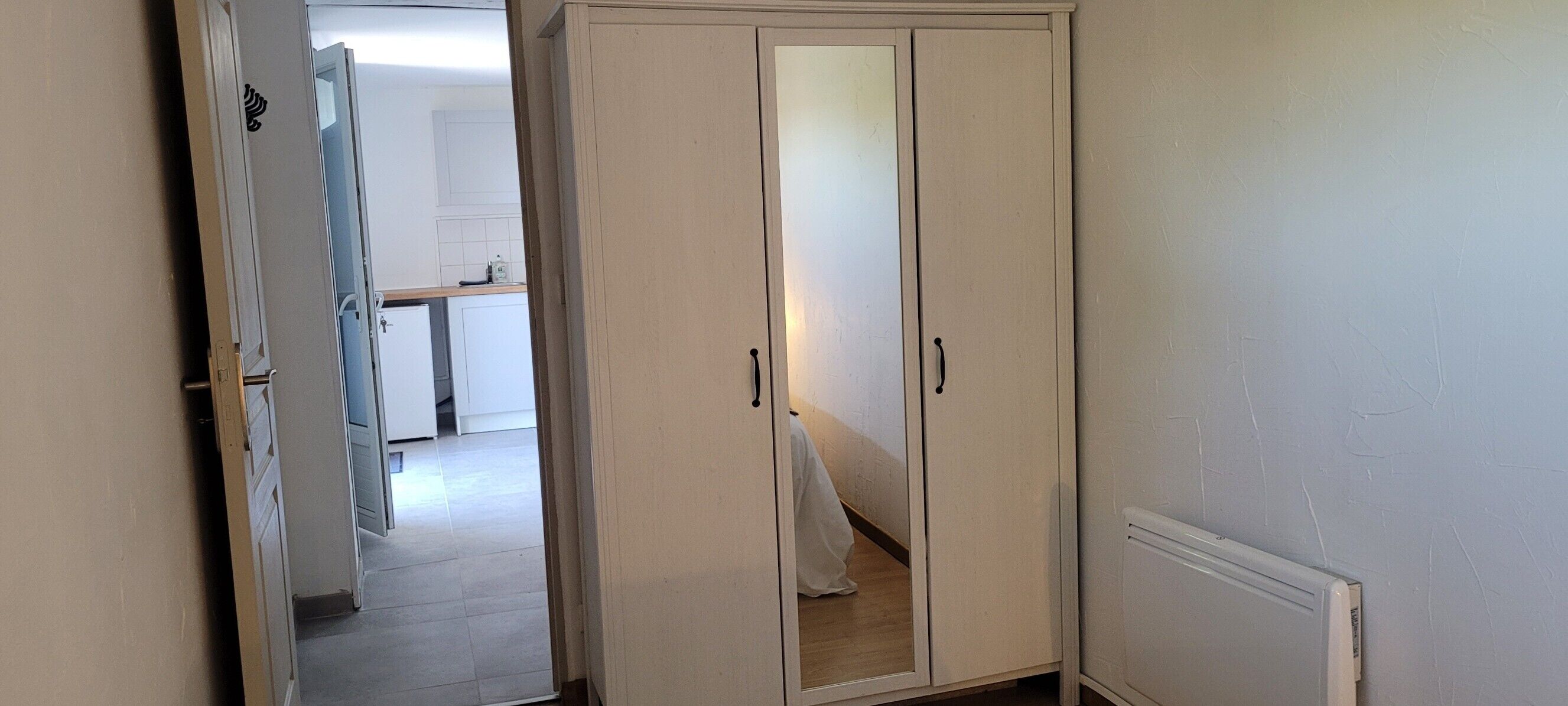 A hallway with a white wardrobe, a radiator, and a glimpse of a kitchen area.