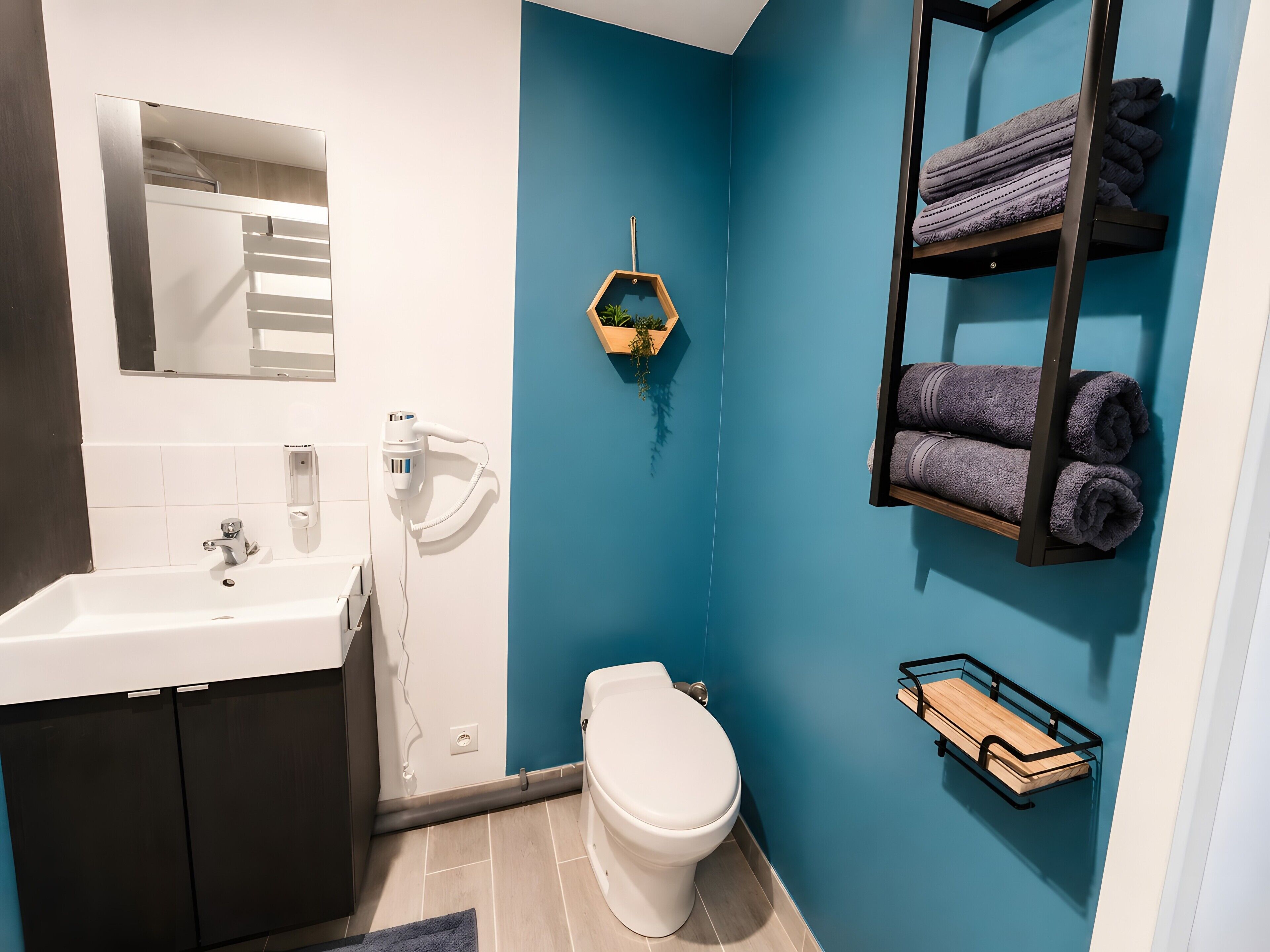 Un baño con un lavabo blanco, un inodoro, un perchero para toallas y un estante con toallas.