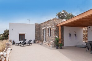 Une maison moderne avec une façade en pierre, un patio couvert doté de chaises longues et une vue sur le paysage environnant.