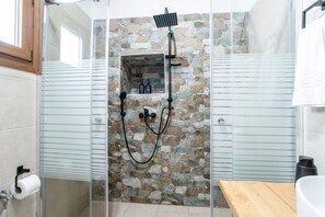 Une douche avec un mur en pierre, un banc en bois et une porte en verre.