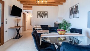 Et moderne spiseområde med et glasbord, mørke polstrede stole, et træloft og et fladskærms-TV monteret på væggen.