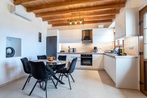 Una cocina moderna con vigas de madera en el techo, un comedor con sillas negras y un horno empotrado.