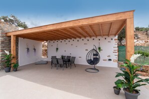 A covered patio area with a table and chairs, potted plants, and a hanging chair.