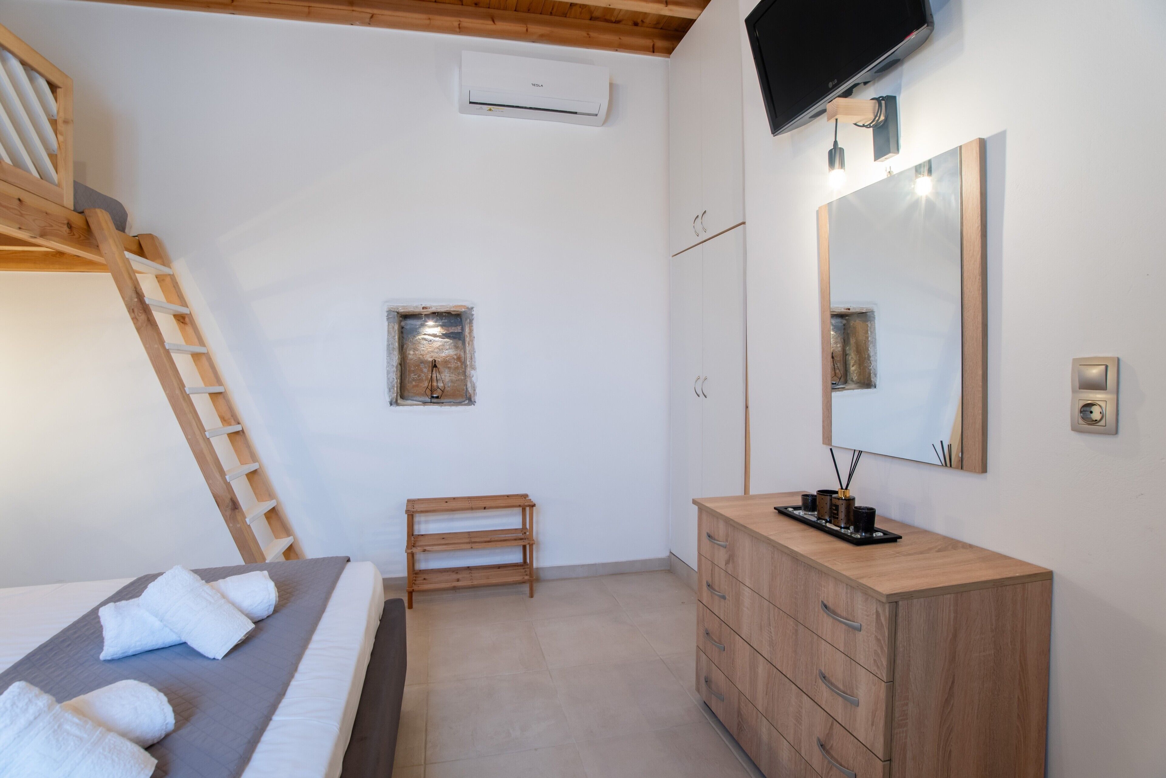 Ein Schlafzimmer mit Etagenbett, einem hölzernen Schminktisch, einem Spiegel und einem an der Wand befestigten Fernseher.