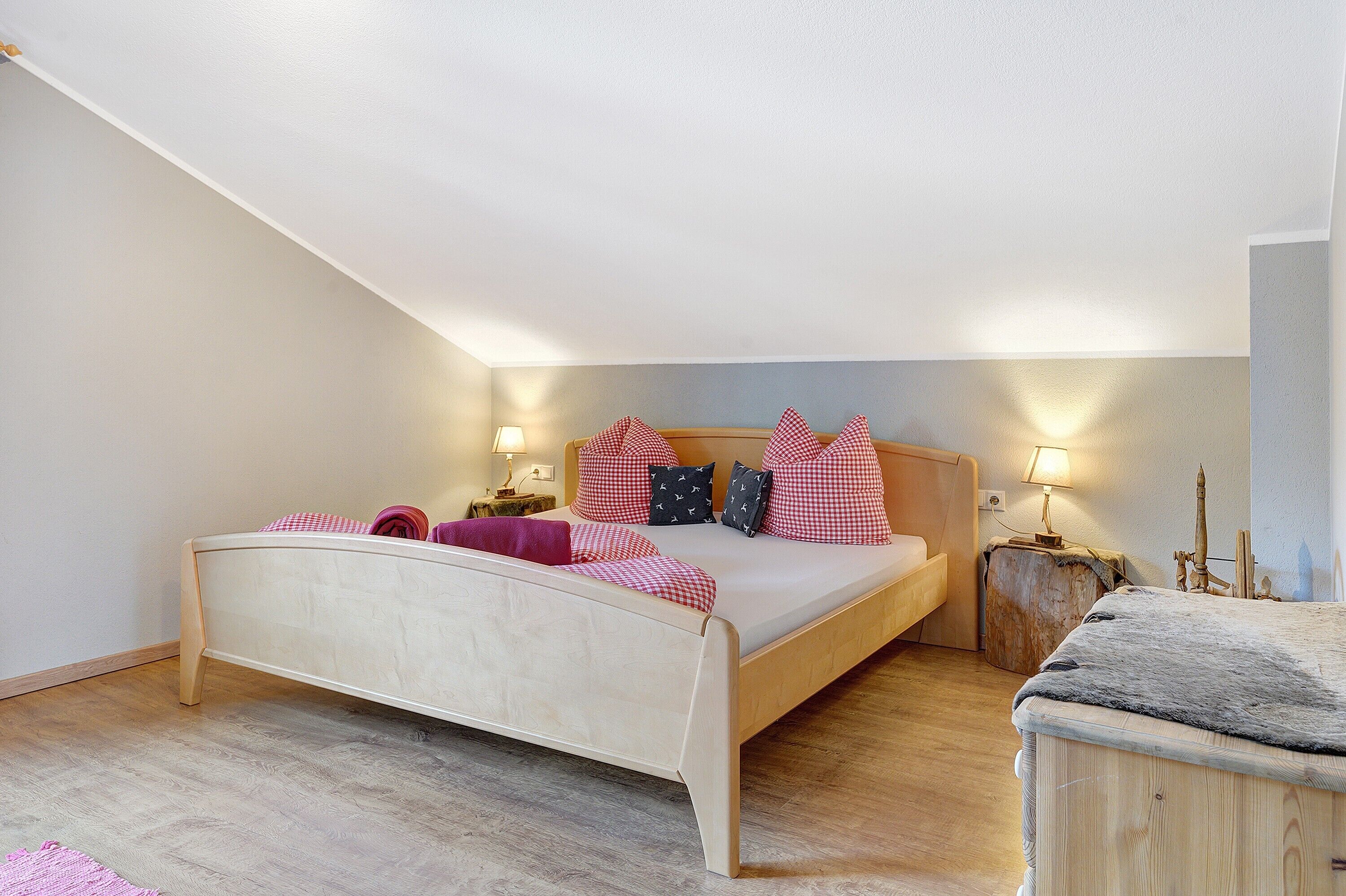 Ein Schlafzimmer mit einem hölzernen Bett, einem Nachttisch mit Lampe und einem kleinen Holzschemel.