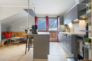 Una cocina moderna con una isla central, banco de madera y vistas a montañas a través de una ventana.