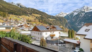 Un pueblo de montaña con casas tradicionales, una cerca de madera y un automóvil estacionado adelante.