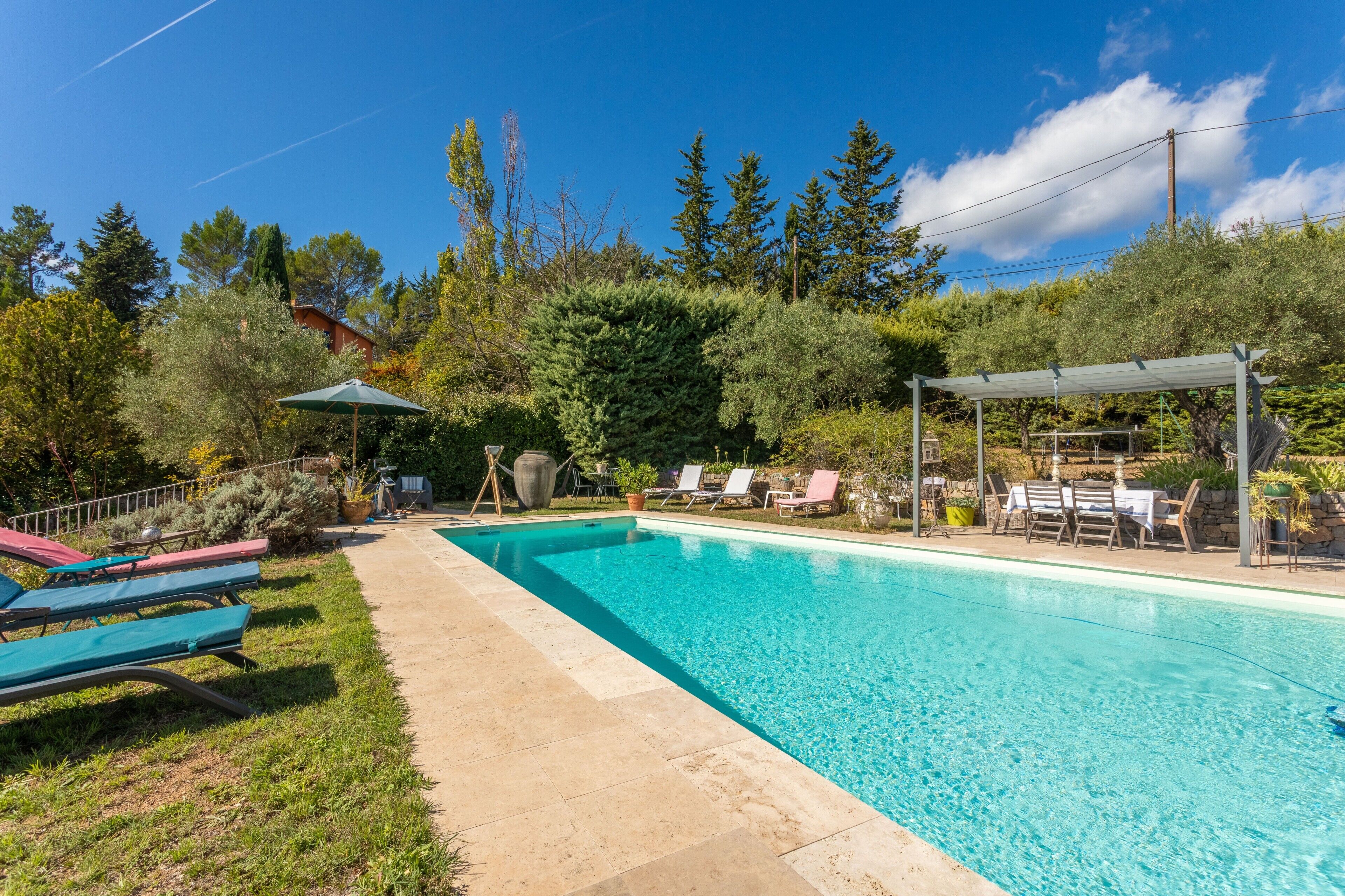 A rectangular swimming pool with a tiled deck, surrounded by lounge chairs and a pergola.