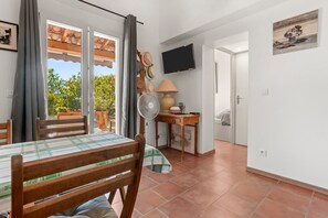 Une pièce comprenant une table à manger, des chaises, un ventilateur, une lampe, un téléviseur et une porte donnant sur une autre pièce.
