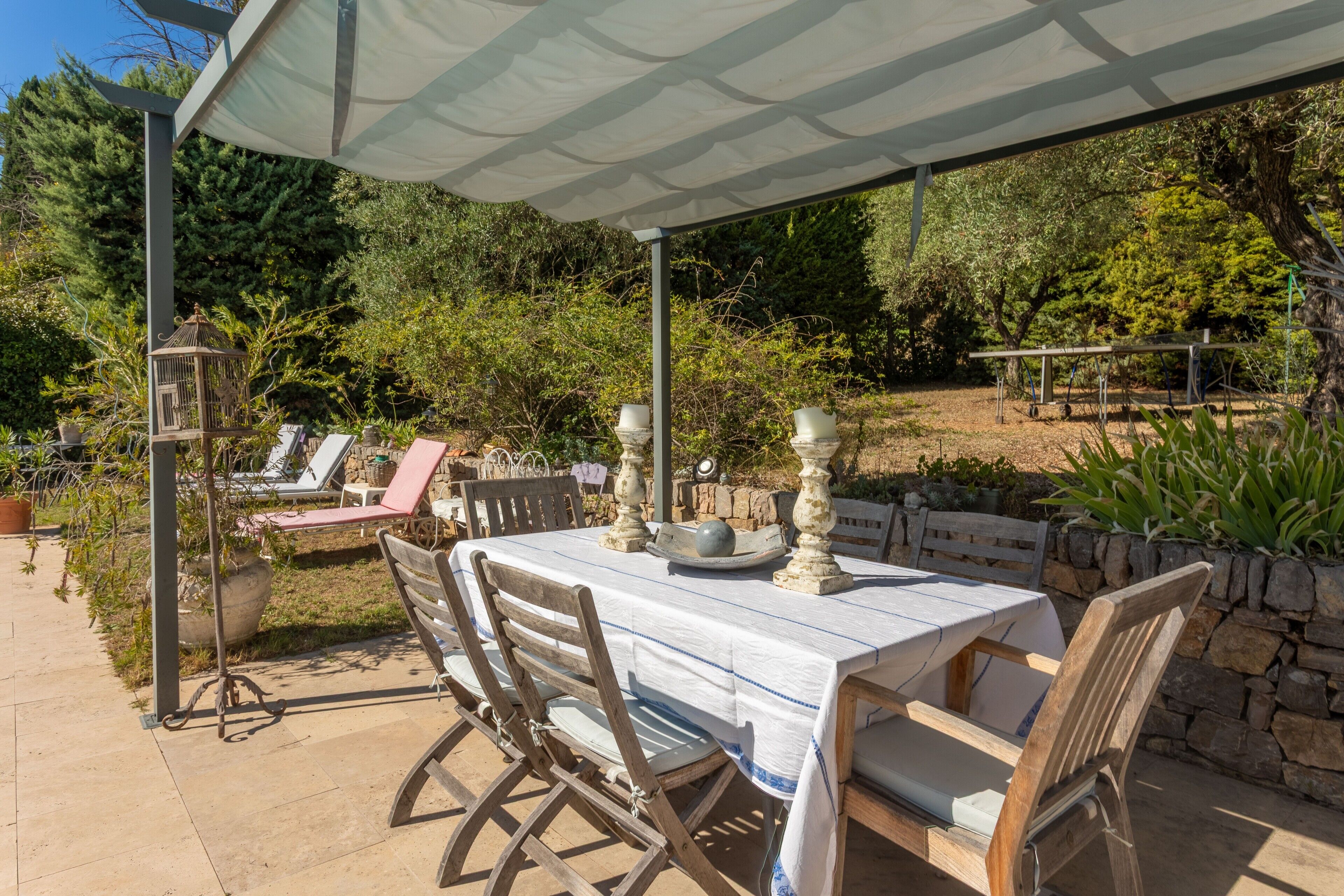 Une terrasse extérieure avec une table et des chaises, entourée de verdure et d’un mur en pierre.