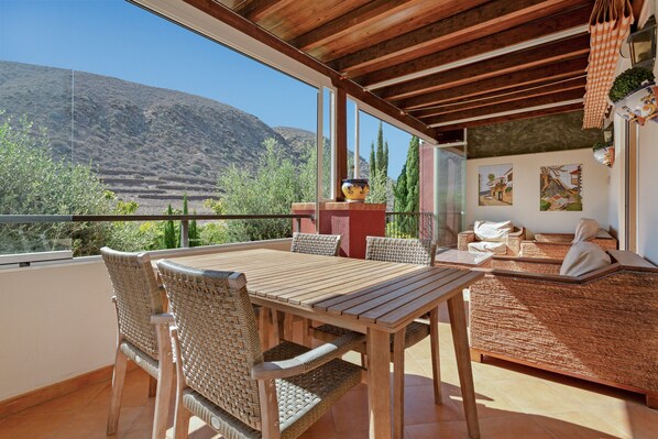 A wooden table and chairs on a balcony with a view of a mountainous landscape.