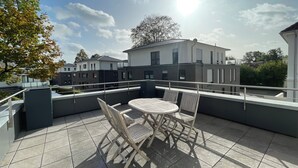 A rooftop terrace with a table and chairs, a view of buildings, and a clear sky.