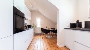 A modern kitchen with white cabinetry, a wooden floor, a dining area with black chairs, and a window providing natural light.