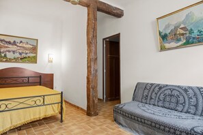 Quarto com cama, sofá, viga de madeira, um quadro e uma porta.
