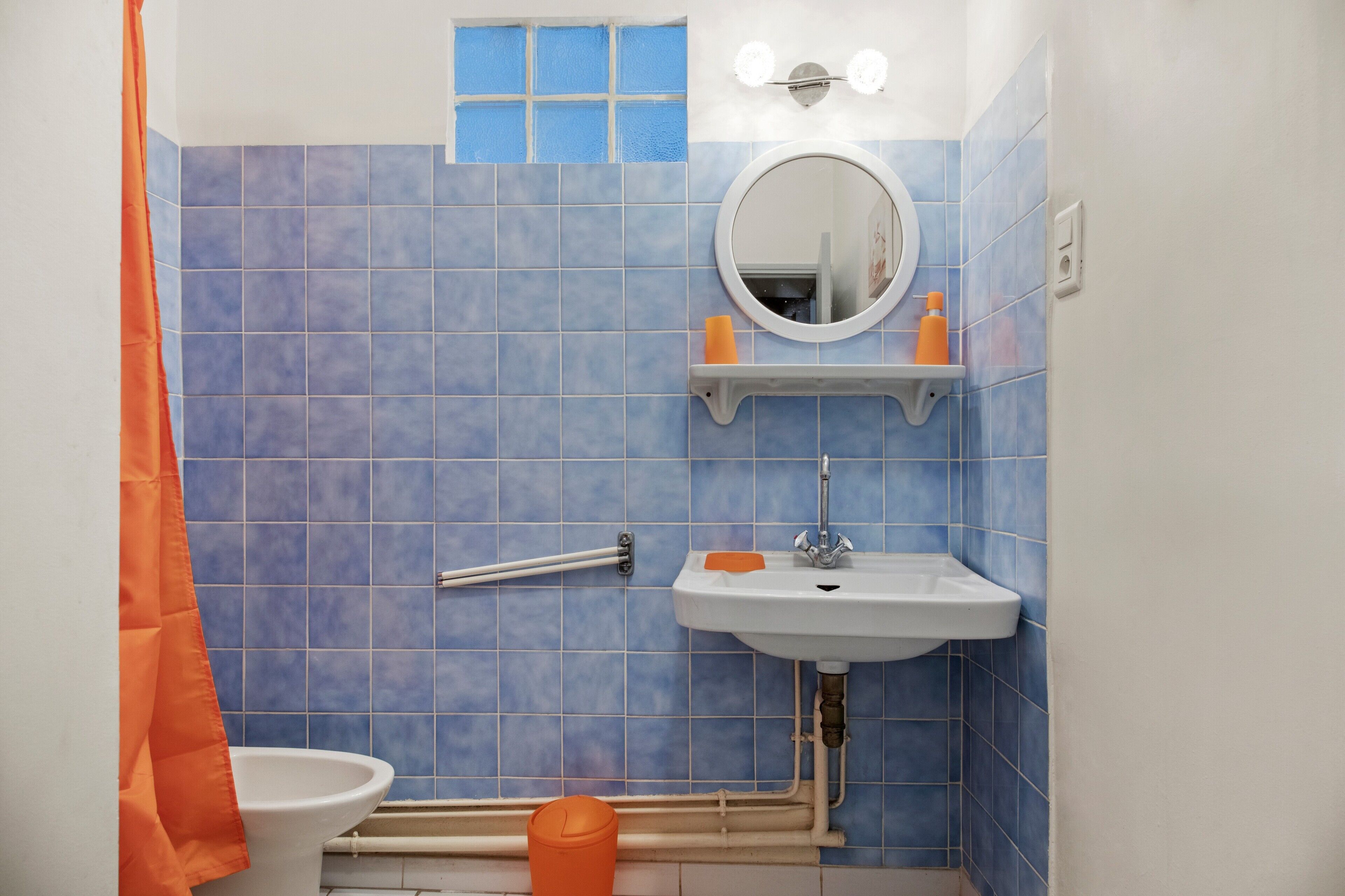 Un baño con azulejos azules, un lavabo blanco, un espejo y una cortina de ducha naranja.