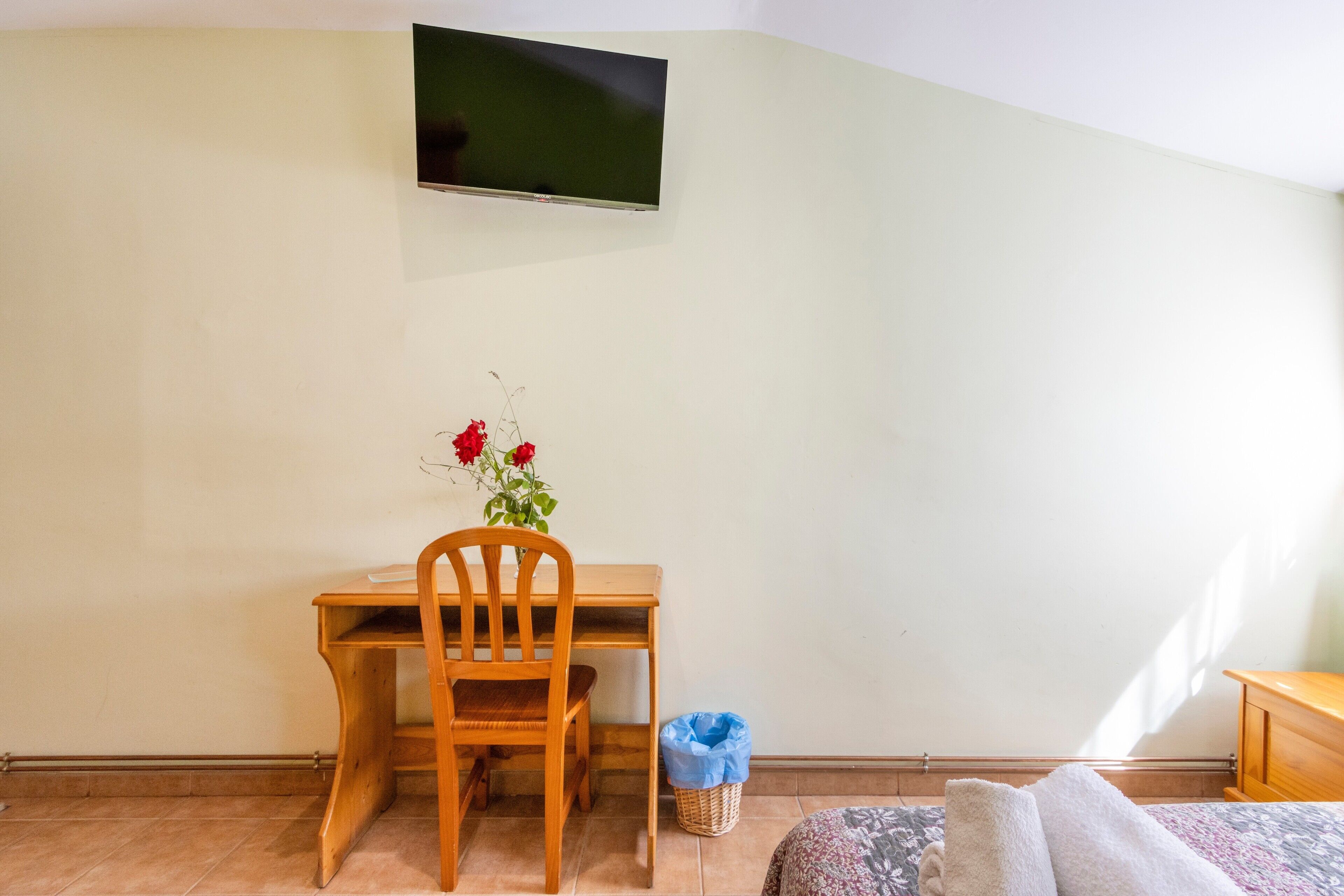 Una habitación con un escritorio de madera, una silla y un televisor fijado a la pared.