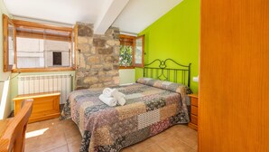 Un dormitorio con pared de piedra, pared verde, cabecero de madera, colcha acolchada, banco de madera y una ventana con persianas.