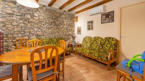 Un comedor con pared de piedra, vigas de madera en el techo, una mesa redonda de madera y sofás estampados.