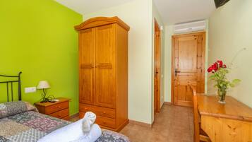 A bedroom with a bed, a wooden wardrobe, a nightstand, a desk, and a chair.