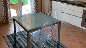 A modern kitchen with a glass dining table, clear chairs, and a view of a dog outside. - Apartment 'Lampone' with Mountain View, Private Terrace and Wi-Fi (Cantello)