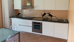 A modern kitchen with white cabinets, a stainless steel range hood, a dishwasher, and a tiled backsplash with a cat-themed design. - Apartment 'Lampone' with Mountain View, Private Terrace and Wi-Fi (Cantello)