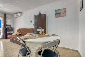 A room with a bed, a small table with chairs, a cabinet, and a wall-mounted air conditioner.