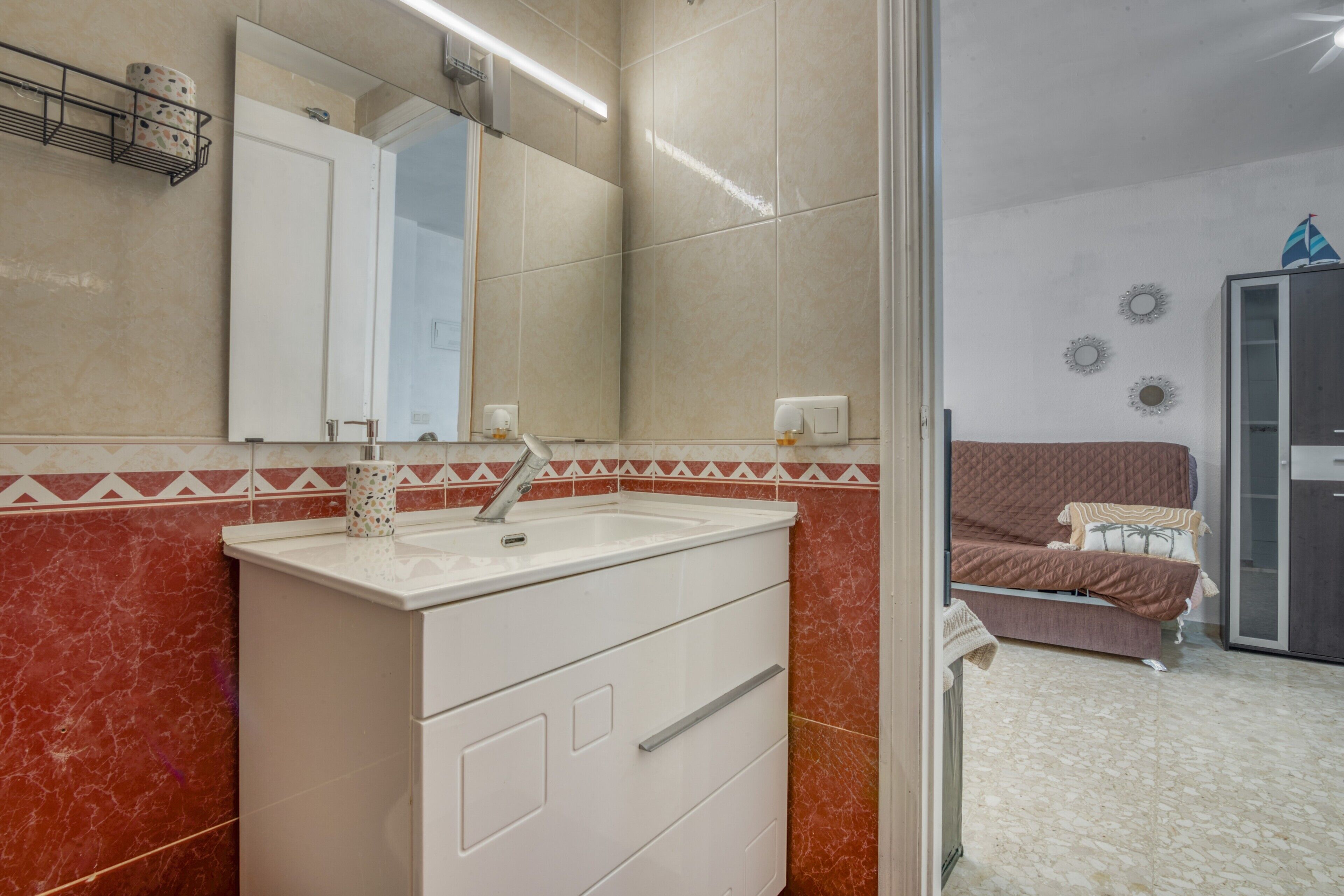Un baño con tocador blanco, espejo y pared con baldosas rojas.