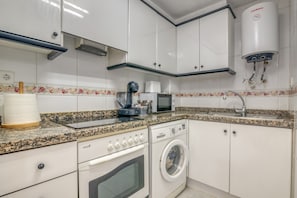 A kitchen with a washing machine, microwave, and a water heater.