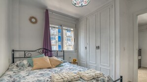 A bedroom with a bed, curtains, a nightstand, and a wardrobe. - Apartment 'On Daimús Beach' with Shared Pool, Wi-Fi and Air Conditioning (Daimús)